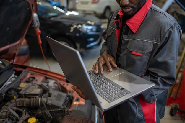 Part of repairman in workwear holding laptop while consulting clients online