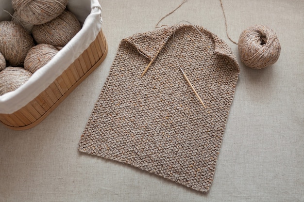 Part of a scarf knitted with circular bamboo needles balls of wool yarn in a basket selective focus