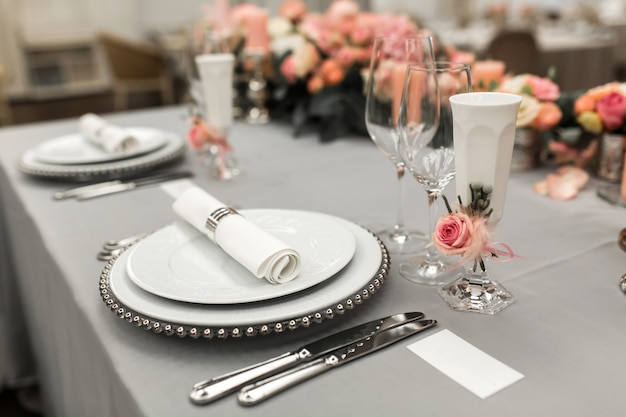 Part of stylish table setting with plate and cutlery. Nearby lies a white business card. Copy space