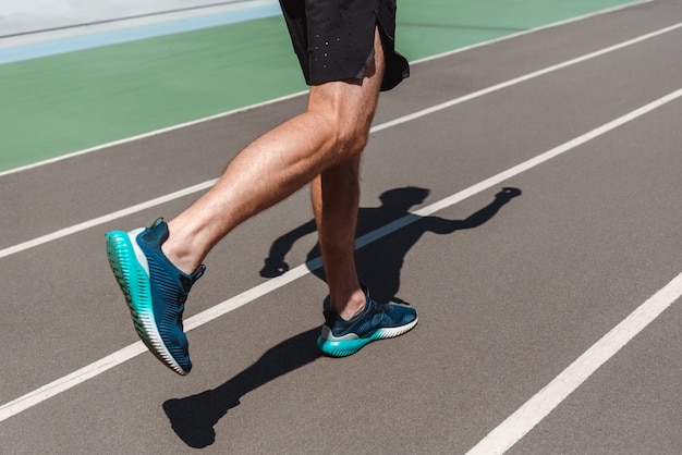 partial view of athletic young sportsman in sneakers jogging on running track