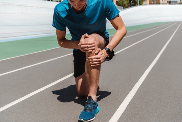 partial view of athletic young sportsman touching leg on running track