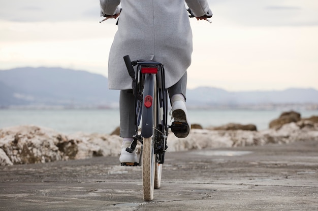 Partial view of bicycle with woman, gray clothes, beach in background. (Focus on bicycle wheel)