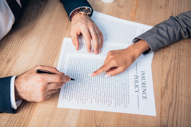 Partial view of lawyer pointing with finger at insurance policy contract near businessman with pen