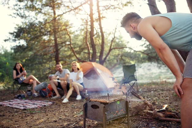 Party, camping of men and women group at forest. They relaxing, singing a song and cooking barbecue against green grass. The vacation, summer, adventure, lifestyle, picnic concept