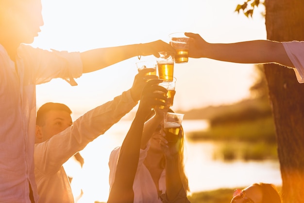 Party Close up hands of friends clinking beer glasses during picnic at the beach in sunshine