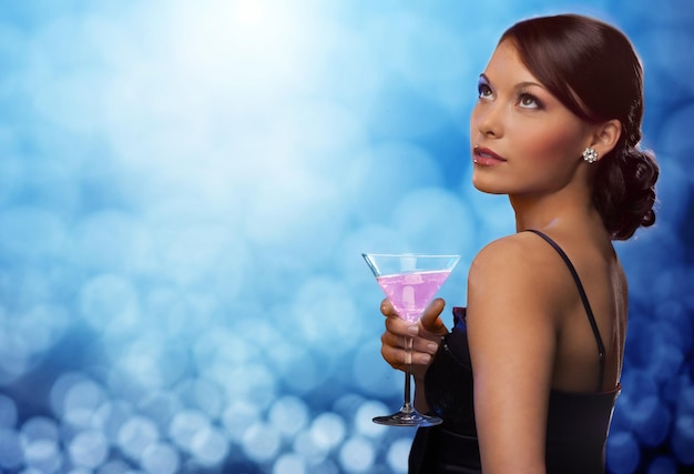 party, drinks, holidays, luxury and celebration concept - smiling woman in evening dress holding cocktail over blue lights background