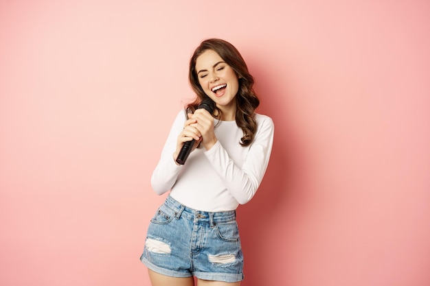 Party girl happy young woman singing in microphone performing song having fun at event standing over...