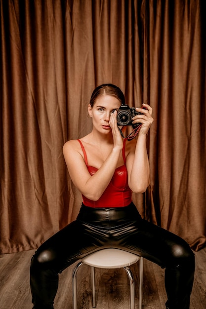 Party girl portrait young woman in red corset and black leather pants with photo camera sexy