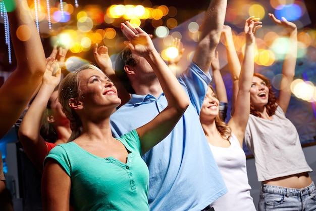 party, holidays, celebration, nightlife and people concept - smiling friends waving hands at concert in club