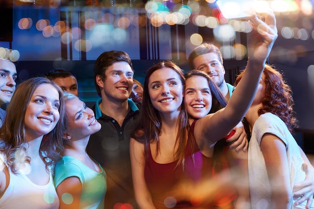 party, technology, nightlife and people concept - smiling friends with smartphone taking selfie in club