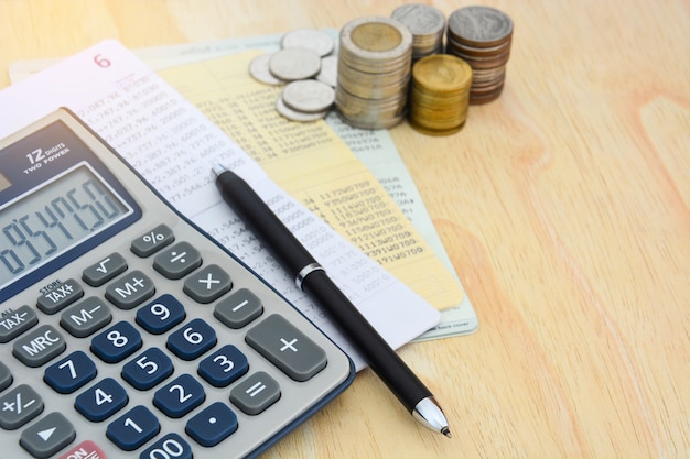 Passbooks saving account, calculator, pen and pile of coins on wooden table background