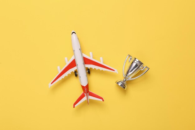 Passenger plane with winners cup on yellow background Top view