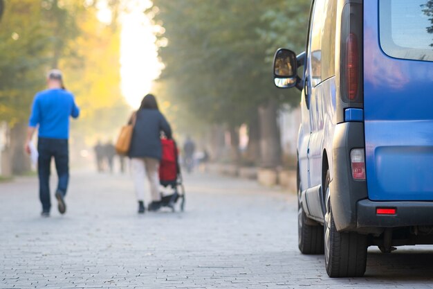 Passenger van car parked on a city alley street side with blurred walking pedestrians in autumn.