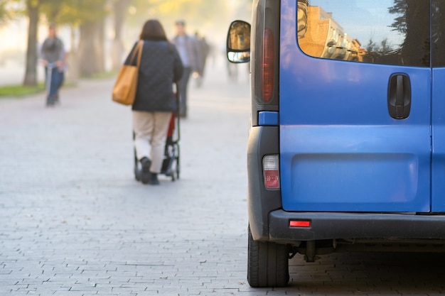 Passenger van car parked on a city alley street side with blurred walking pedestrians in autumn.