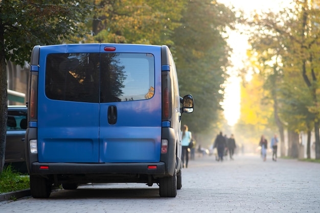 Passenger van car parked on a city alley street side with blurred walking pedestrians in autumn.