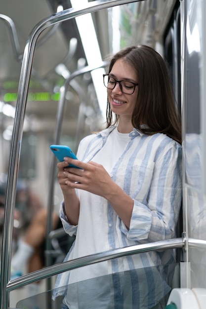 Passenger young woman using mobile smart phone chatting in social networks in subway train at metro