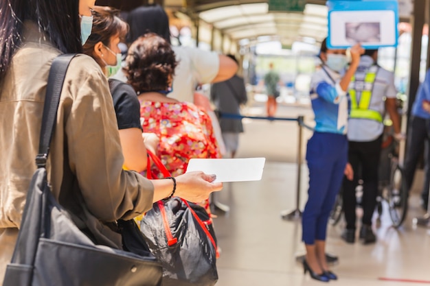 Passengers in medical mask holding boarding pass queueing for departure.