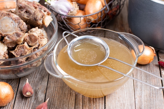 Passing the bone broth through a sieve. Concentrated Bone Broth in a bowl on the table