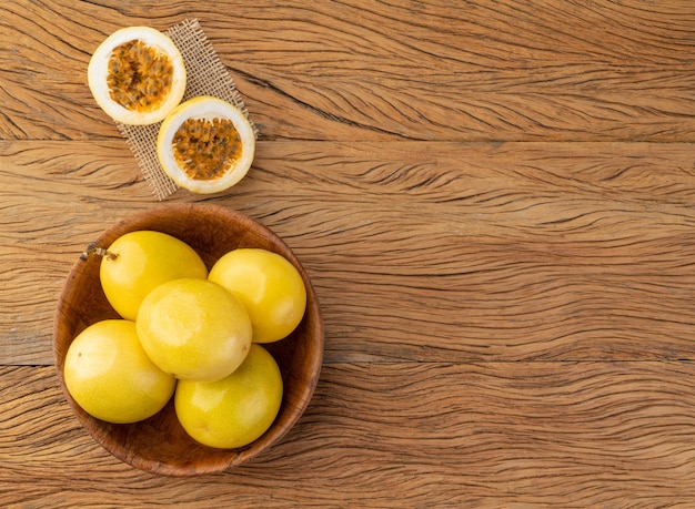 Passion fruits in a bowl with cut fruit over wooden table with copy space