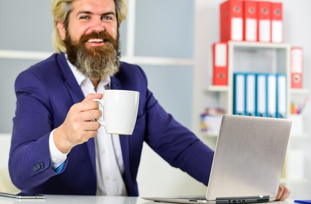 Photo passionate about business goals smiling entrepreneur in modern office business success successful bearded ceo in jacket confident man manager at laptop mature male boss businessman drink coffee