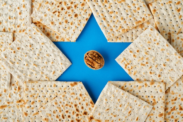 Passover celebration concept Blue Star of David made from matzah white and yellow roses kippah and walnut on bluebackground Traditional ritual Jewish Passover food Pesach Jewish holiday Mock up