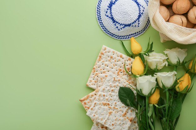 Passover celebration concept Matzah kosher red wine walnut and spring white and yellow rose flowers Traditional ritual Jewish bread on light green background Passover food Pesach Jewish holiday