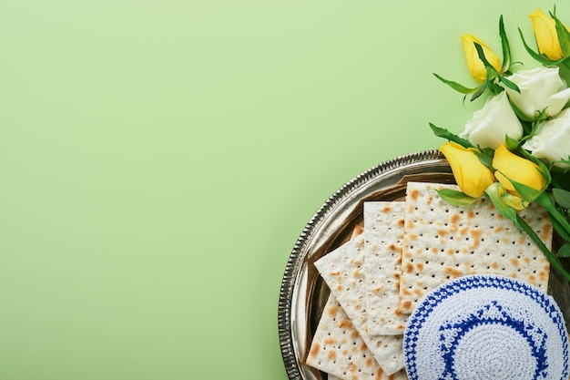 Passover celebration concept Matzah kosher red wine walnut and spring white and yellow rose flowers Traditional ritual Jewish bread on light green background Passover food Pesach Jewish holiday