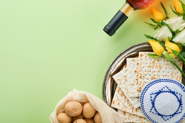 Passover celebration concept Matzah kosher red wine walnut and spring white and yellow rose flowers Traditional ritual Jewish bread on light green background Passover food Pesach Jewish holiday