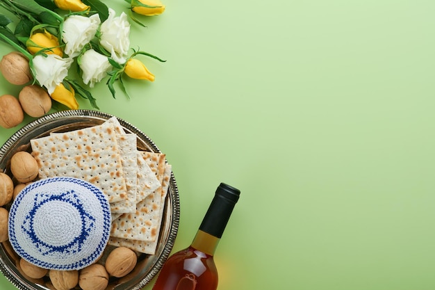 Passover celebration concept Matzah kosher red wine walnut and spring white and yellow rose flowers Traditional ritual Jewish bread on light green background Passover food Pesach Jewish holiday