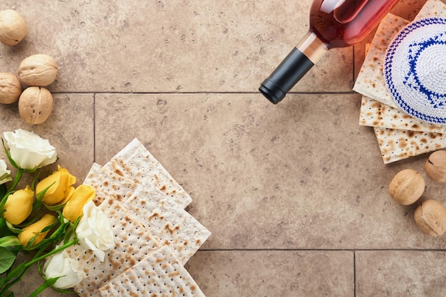 Passover celebration concept Matzah kosher red wine walnut and white and yellow roses Traditional ritual Jewish bread on sand color old tile wall background Passover food Pesach Jewish holiday