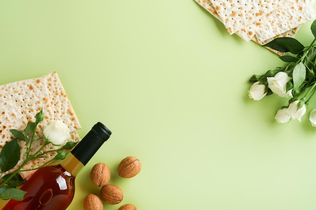 Passover celebration concept Matzah red kosher wine walnut and spring beautiful rose flowers Traditional ritual Jewish bread on light green background Passover food Pesach Jewish holiday