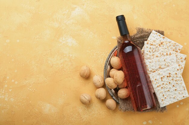 Passover Pesah celebration concept Matzah kosher red wine walnut and white and yellow roses Traditional ritual Jewish bread on sand color old tile wall background Pesach Jewish holiday Top view