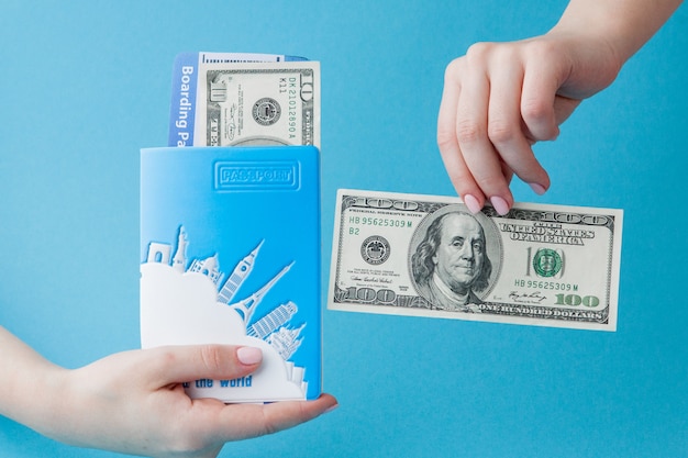 Passport, dollars and air ticket in woman hand on a blue background. Travel concept, copy space