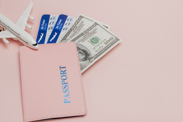 Passport, dollars, plane and air ticket on a pink background. Travel concept, copy space.