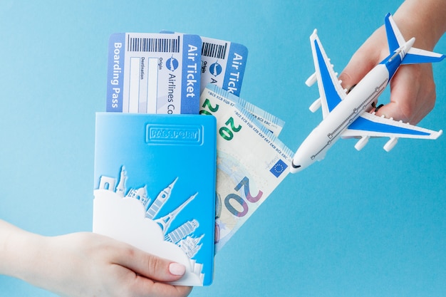 Passport, euro, plane and air ticket in woman hand on a blue background. Travel concept, copy space