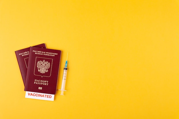 Passports with vaccinated stamp on blank syringe with vaccine on yellow surface