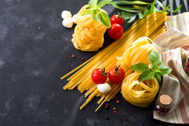 Pasta background. Several types of dry pasta with vegetables and herbs on a dark stone tab