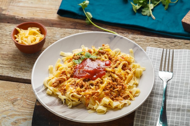 Pasta bolognese garnished with greens and cheese in a plate on a wooden table next to a fork