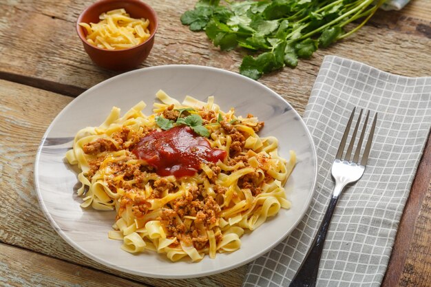 Pasta bolognese garnished with herbs and cheese in a plate on a wooden table next to a fork