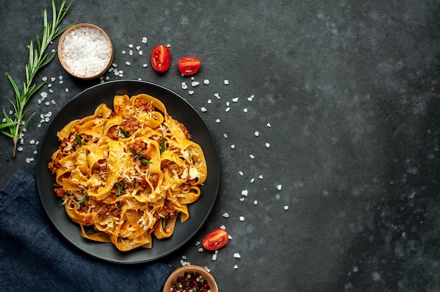 Pasta Bolognese with spices, Italian pasta dish with minced meat and tomatoes in a dark plate on a stone background