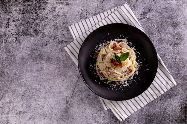 Pasta Carbonara. Spaghetti with bacon, parsel and parmesan cheese. Pasta Carbonara on black plate with parmesan. Italian food.