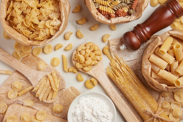 Pasta concept some types of pasta being organized on wooden spoons and in paper bags