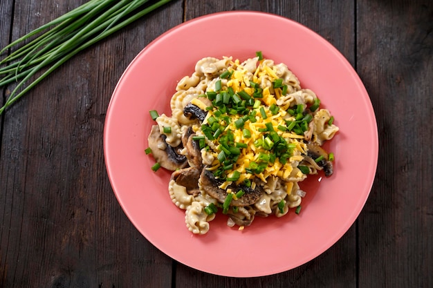 Pasta in a creamy sauce with mushrooms in a plate on the table next to green onion feathers