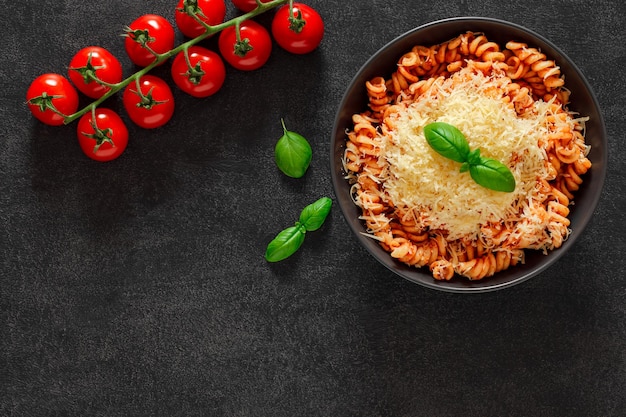 Pasta fusilli cooked with tomato sauce and grated parmesan and cherry tomatoes branch on dark background top view space to copy text