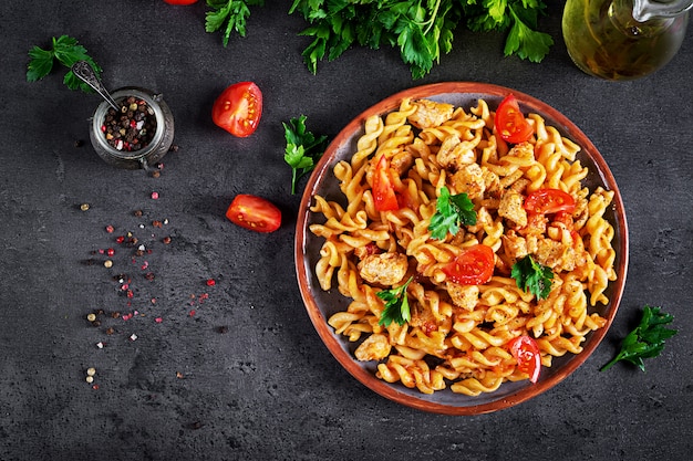 Pasta Fusilli with tomatoes, chicken meat and parsley on plate on dark table