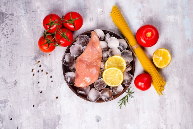 Pasta ingredients. Chicken breasts, tomatoes, spaghetti pasta, and lemon on the stone table.