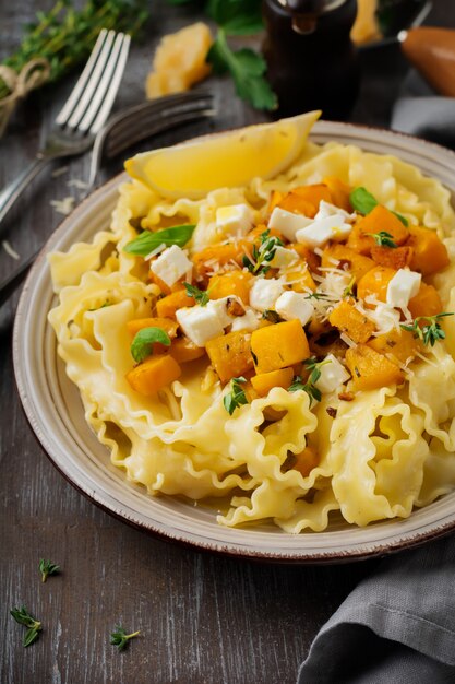 Pasta Mafaldine Napoletane with baked pumpkin, feta cheese and seasoning herbs in ceramic plate. Rustic style. Top view.