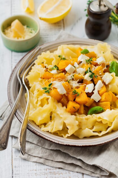 Pasta Mafaldine Napoletane with baked pumpkin, feta cheese and seasoning herbs in ceramic plate on white wooden table. Rustic style. Top view.