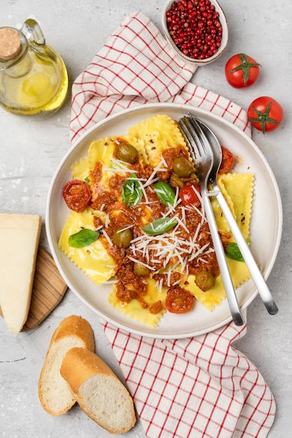 Pasta ravioli with tomato sauce and olives with basil and cheese on a gray background