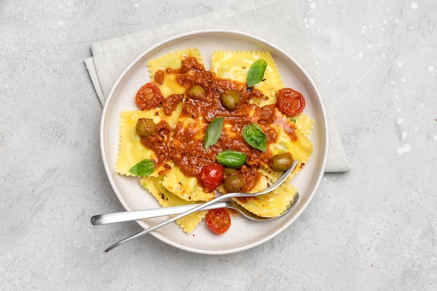 Pasta ravioli with tomato sauce and olives with basil and cheese on a gray background